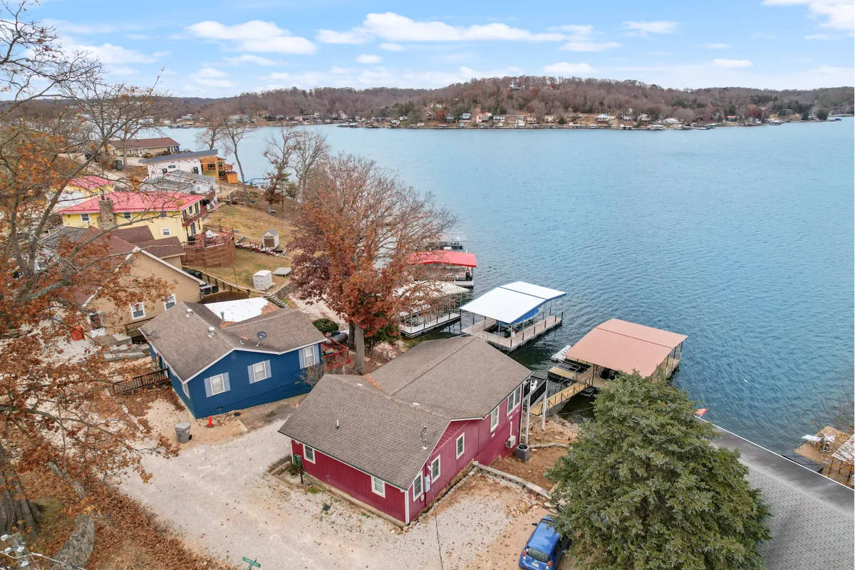 A relaxed exterior image showcasing colorful houses, a dock extending over the lake, and surrounding trees. The setting is ideal for family gatherings, swimming, and picnicking, with a lively and inviting lakeside atmosphere.
