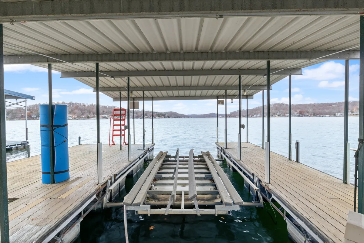 This image showcases a serene waterfront scene with a dock extending over the water, a red safety ladder, a blue foam swim mat, and mountainous scenery in the background. The dock appears sturdy and well-equipped for various activities, with visible space for boats to dock and people to relax or prepare for swimming.
