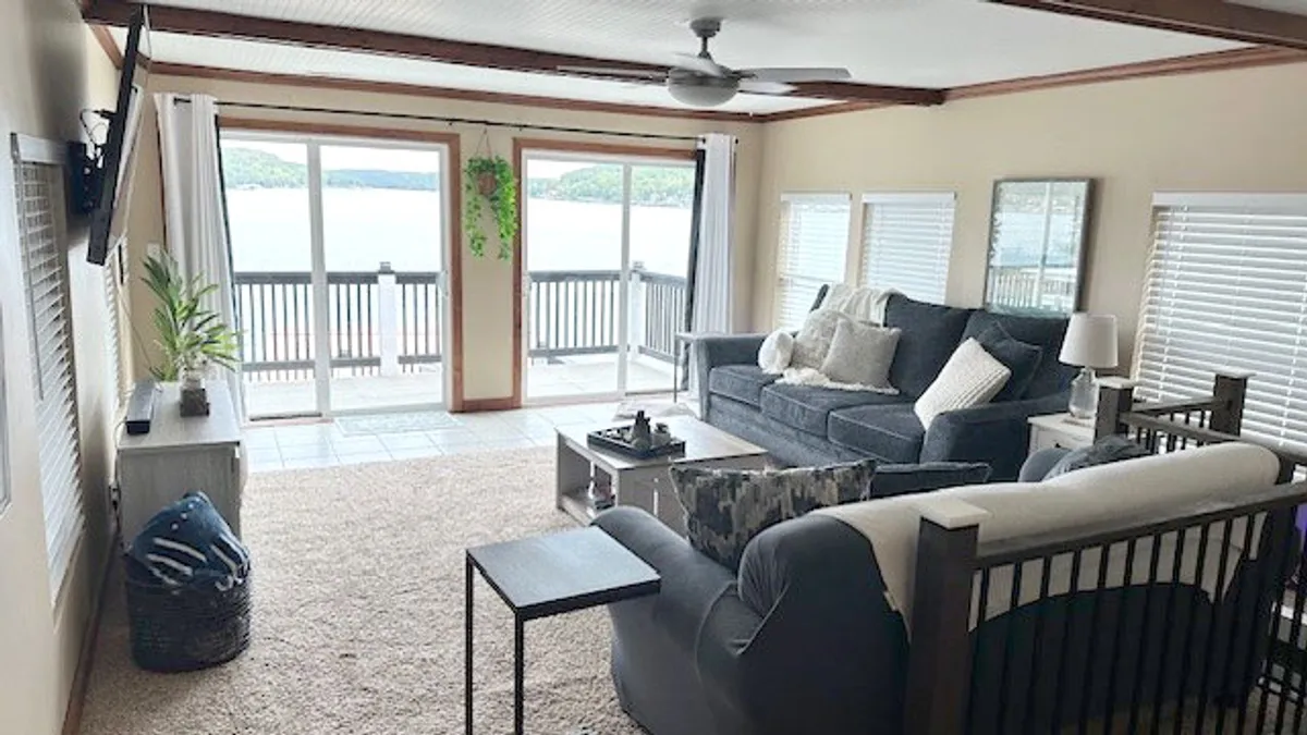 A spacious living room with large windows offering sweeping lake views. Comfortable seating, decorative plants, and a tranquil ambiance make this area ideal for relaxing or socializing with friends and family.