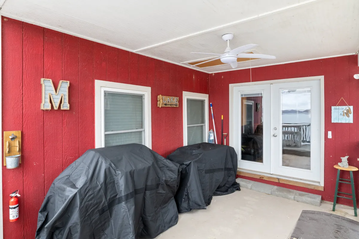 A casual, cozy indoor-outdoor grilling area featuring red paneled walls, covered outdoor grills, and a window framing the lake view. The space is ready for barbecues or morning coffee on the porch, ideal for gathering and entertaining.