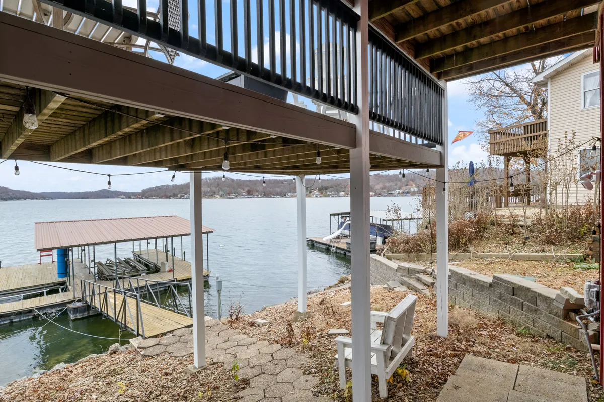 A peaceful scene showing the lakeside dock, clear water, and under-deck patio seating. The image also reveals outdoor seating areas ideal for relaxation and socializing, with the dock just steps away for easy water access.