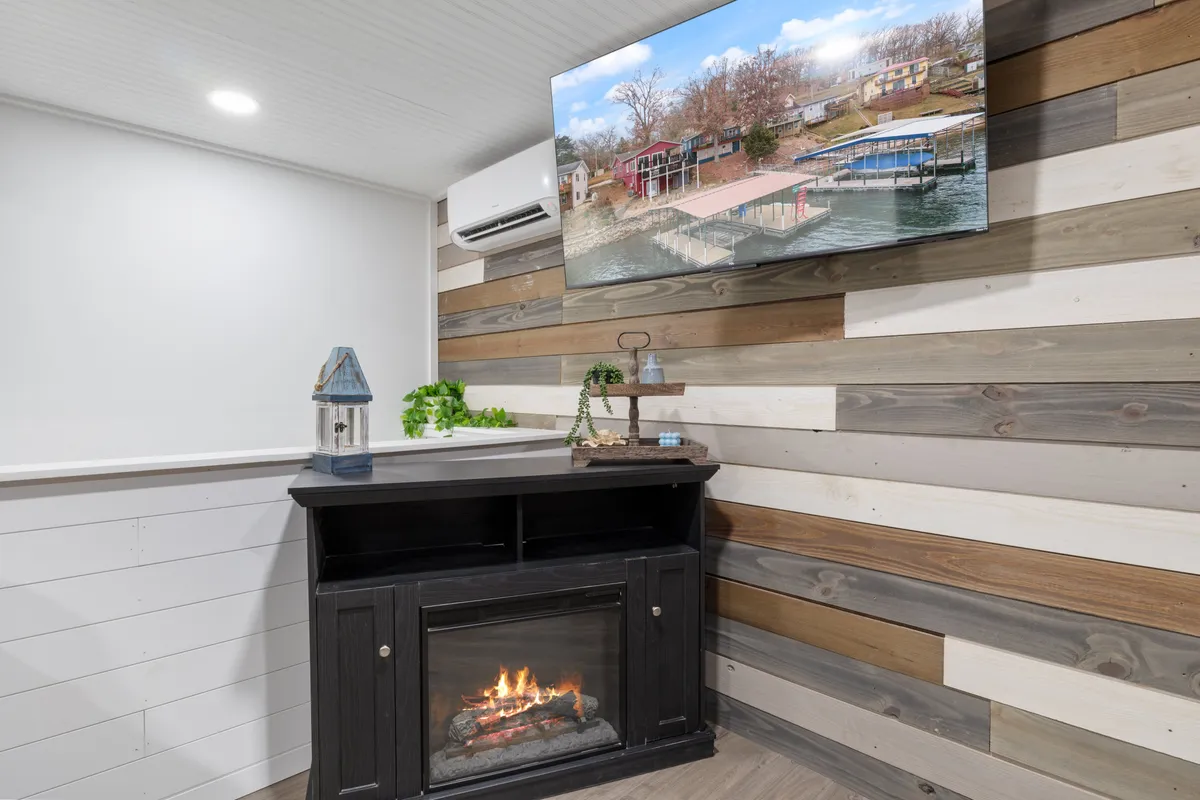 A cozy interior with a fireplace, TV displaying a scenic view, and warm wooden wall paneling. The inviting atmosphere is perfect for curling up with your partner, enjoying a quiet drink, or relaxing by the fire after a day outdoors.