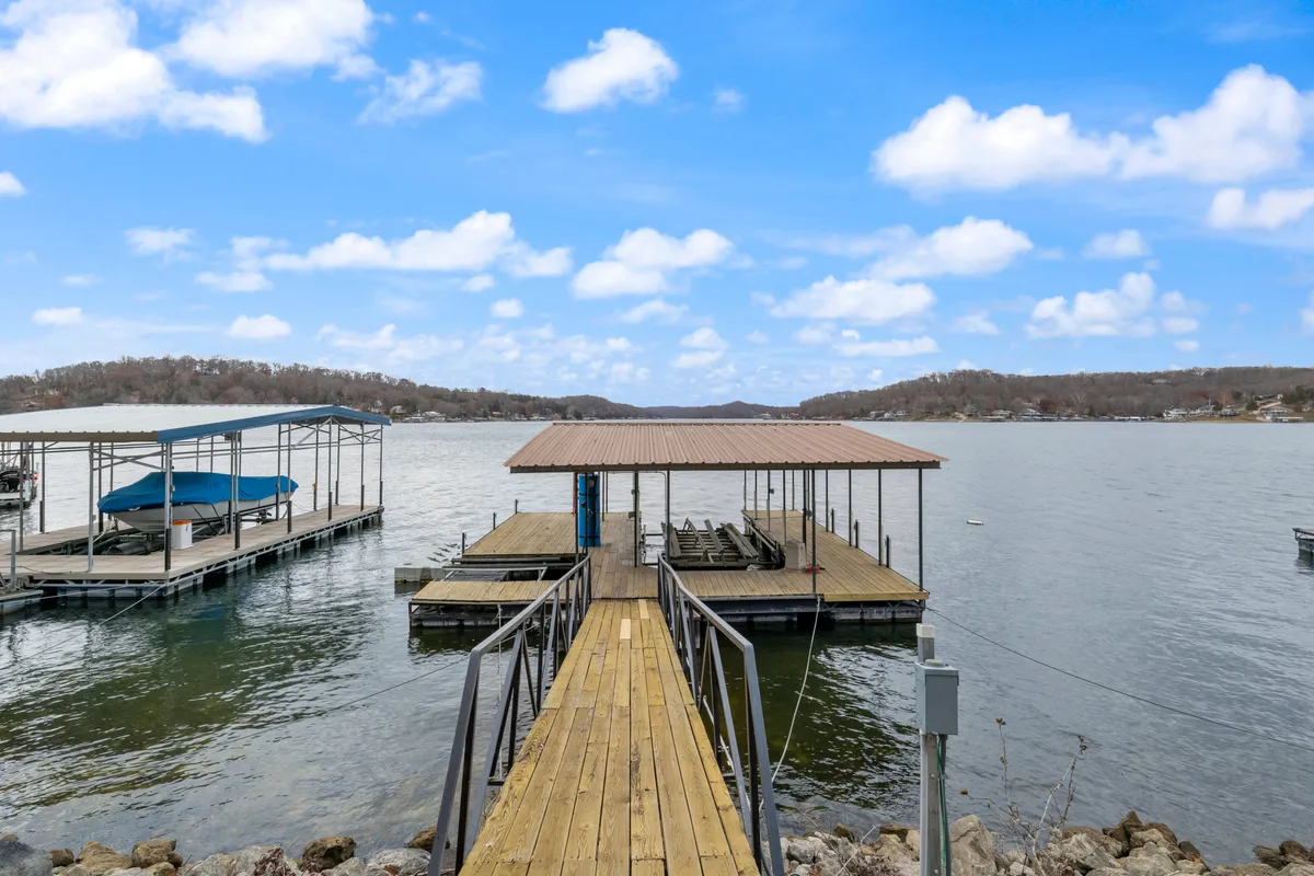 This image features a picturesque exterior view of a lakeside dock, boats, calm water, and rolling hills in the background. The dock is spacious and accessible, inviting families and groups to gather for swimming, fishing, boating, or simply relaxing by the water.