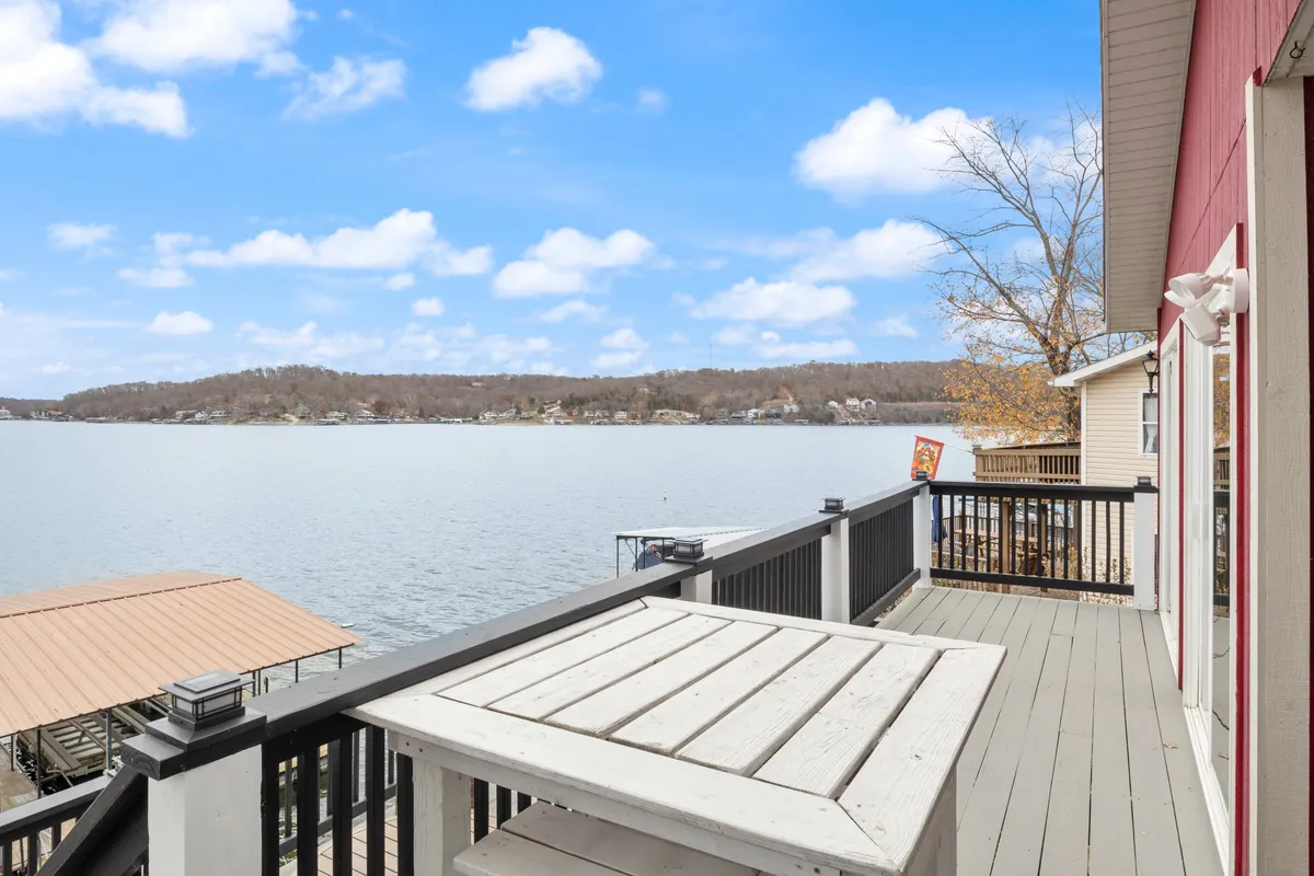 A serene deck area overlooking the lake, surrounded by trees. The tranquil setting offers a perfect spot for morning coffee or relaxing with a book, with the lake as a constant presence.