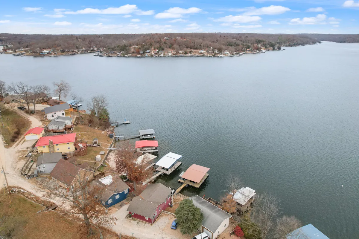 A wide lake view with boathouses, houses nestled among trees, and shimmering water reflecting the soft glow of late afternoon or sunset. The scene invites thoughts of peaceful boating, fishing, or simply soaking in the view with a loved one.